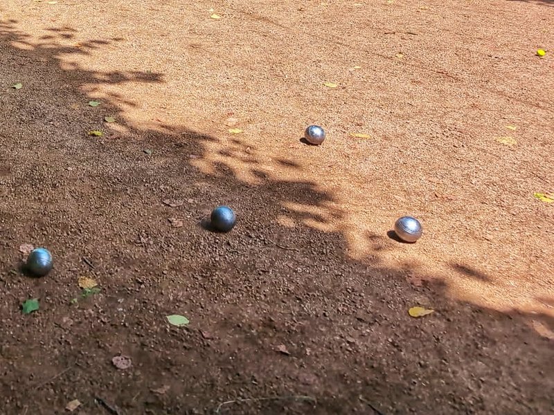 Pétanque boules scattered across a sunlit gravel court.