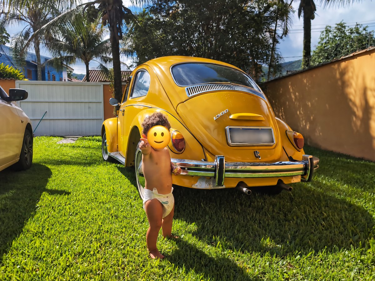 A yellow Volkswagen Beetle parked beneath palm trees.
